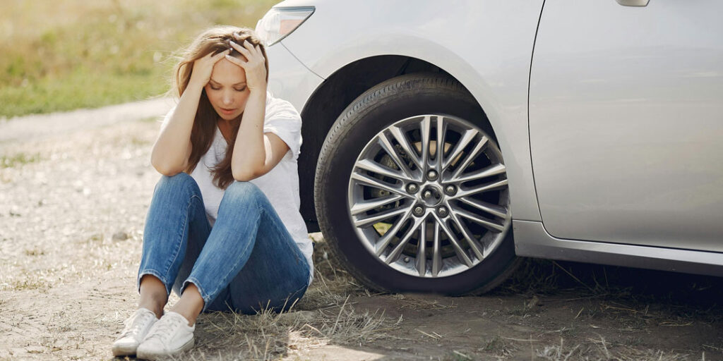 A woman sitting in front of a white car