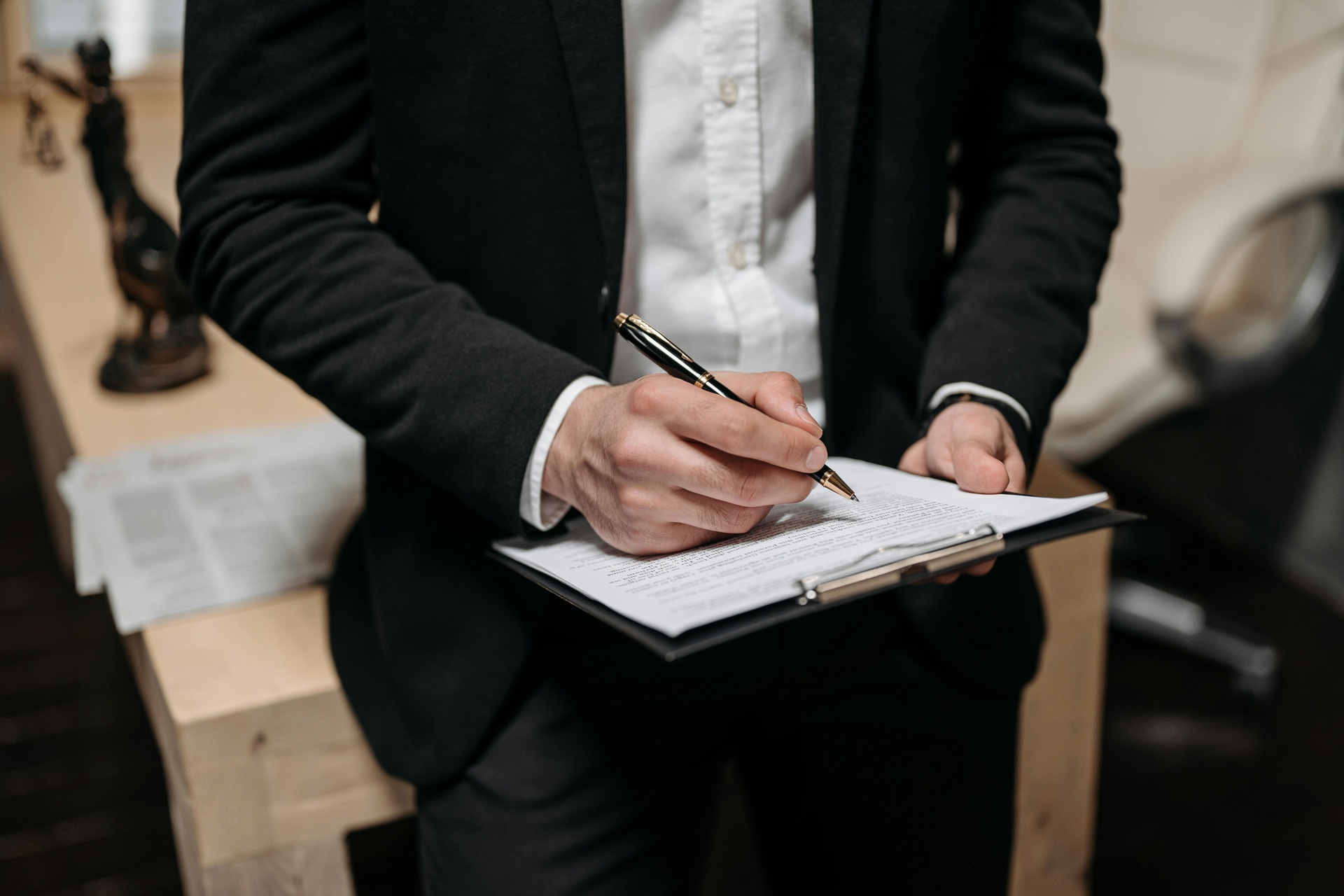 Person in a black suit writing on a clipboard with a premium black and gold pen Person in a black suit writing on a clipboard with a premium black and gold pen