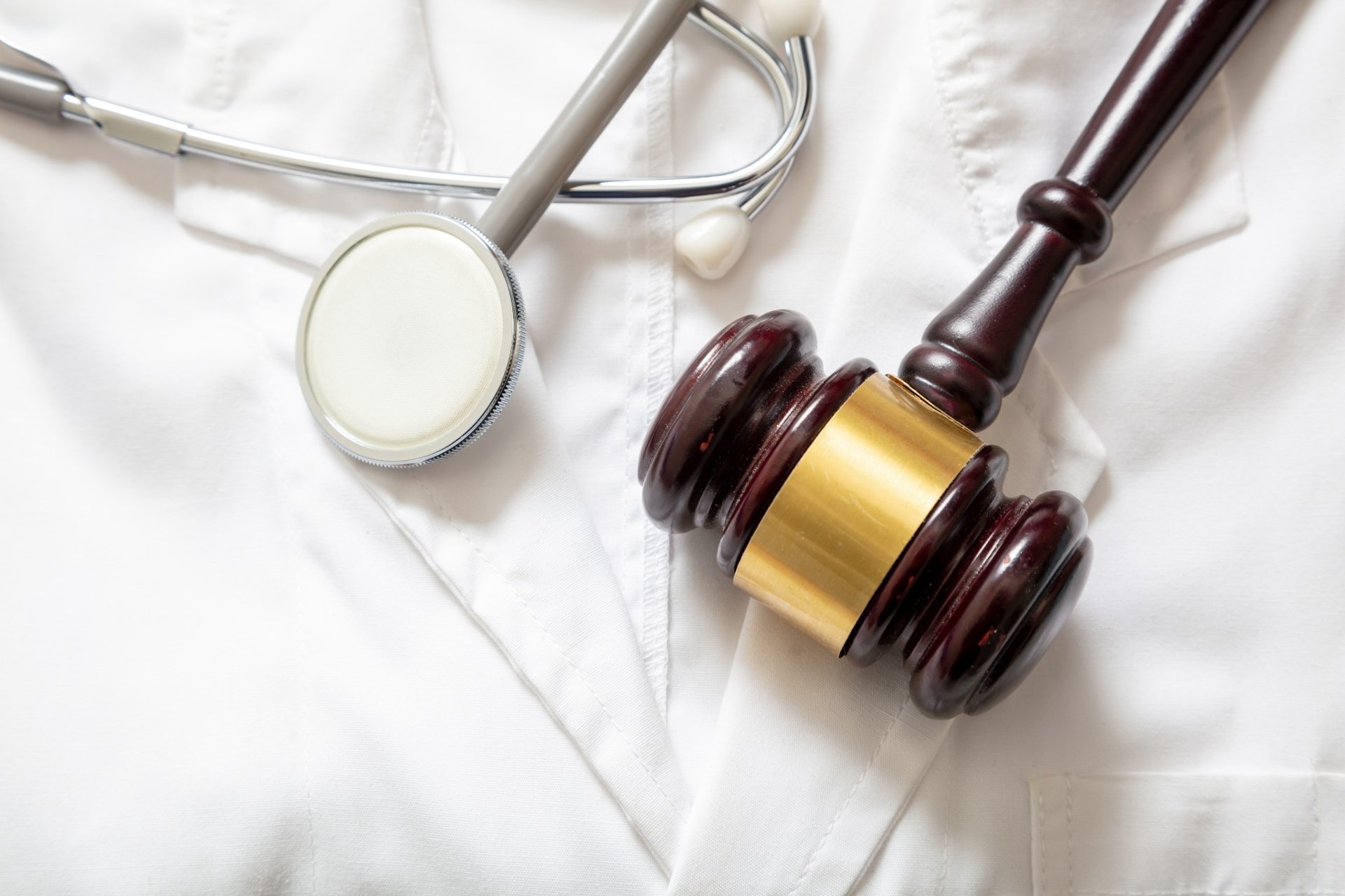 Close-up of stethoscope and judge's gavel on a white medical coat Close-up of stethoscope and judge's gavel on a white medical coat