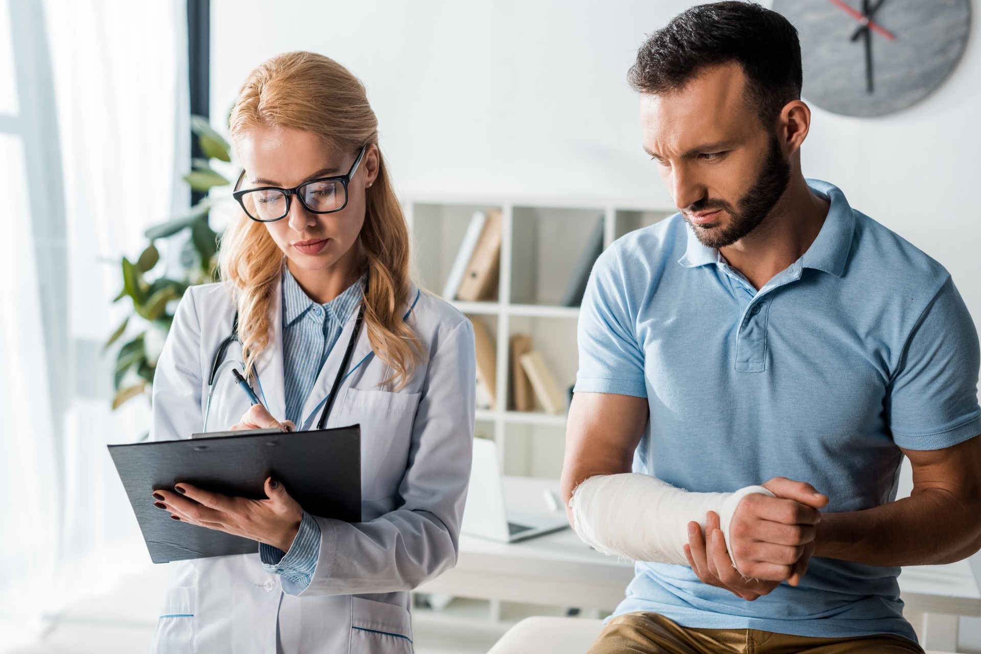 Doctor taking notes while examining patient with arm cast Doctor taking notes while examining patient with arm cast