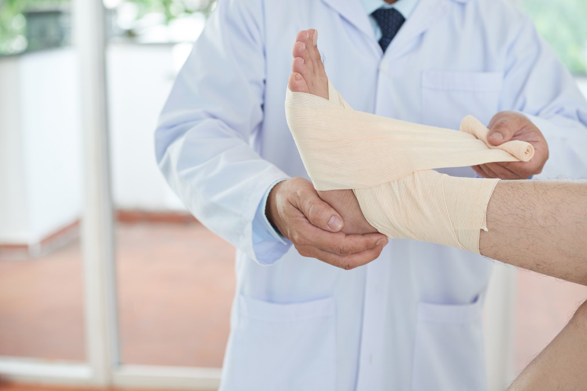 Doctor wrapping elastic bandage around patient’s injured ankle Doctor wrapping elastic bandage around patient’s injured ankle
