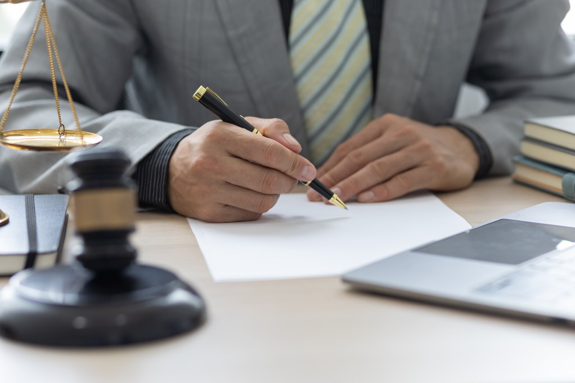 Lawyer writing on paper at desk with gavel and scales