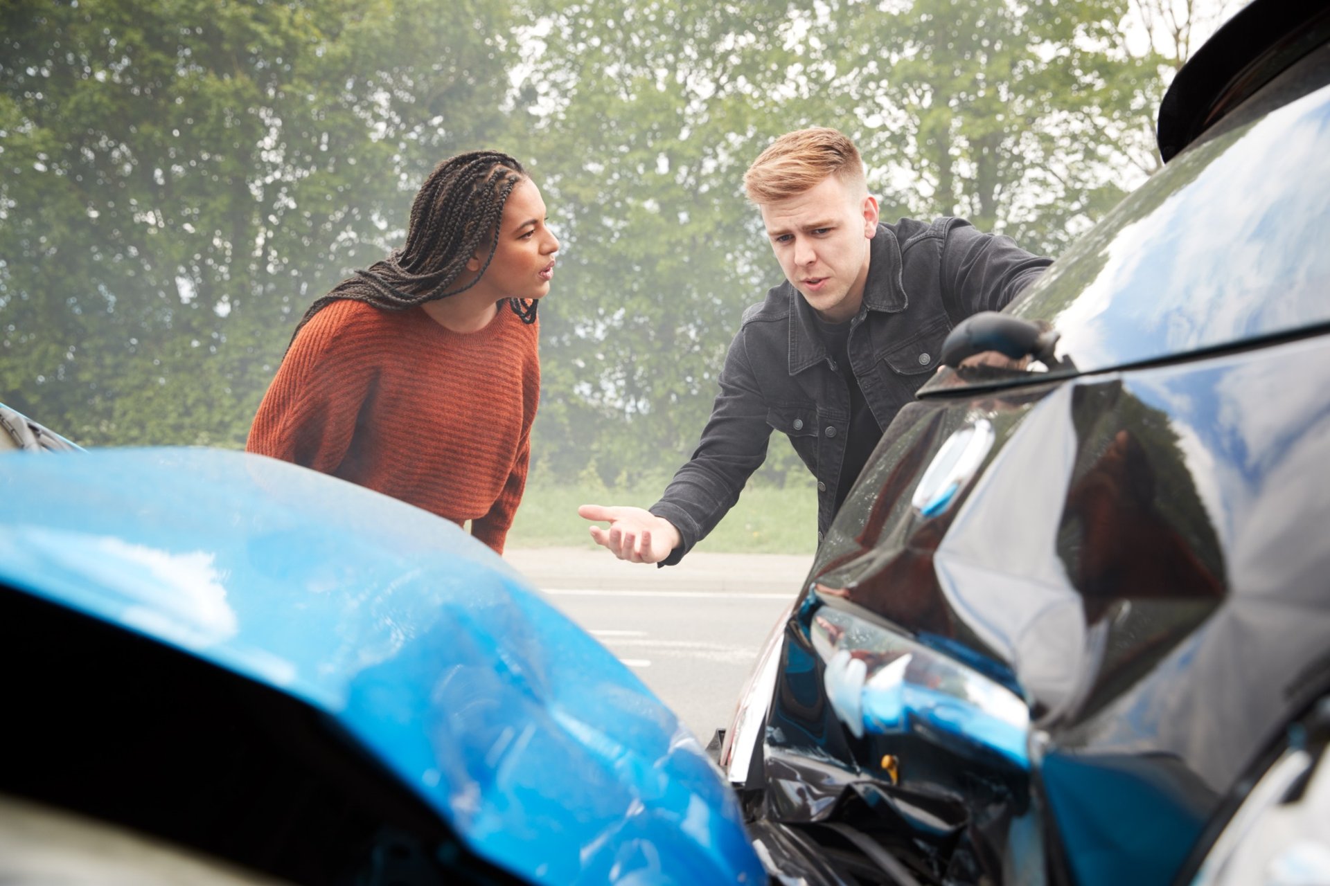 Two drivers arguing beside their damaged vehicles after an accident Two drivers arguing beside their damaged vehicles after an accident