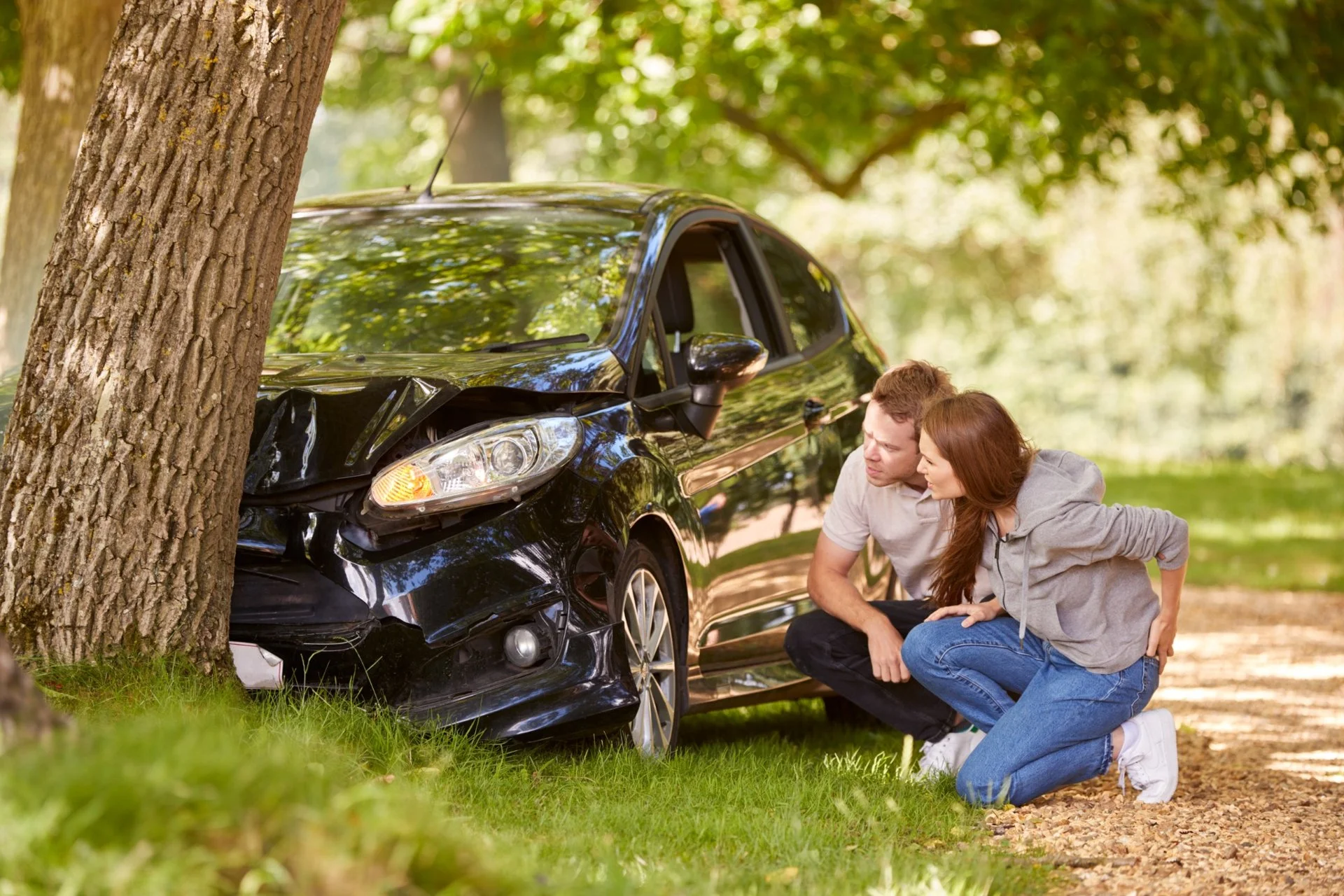 Couple examining damage after their car crashed into a tree in a wooded area