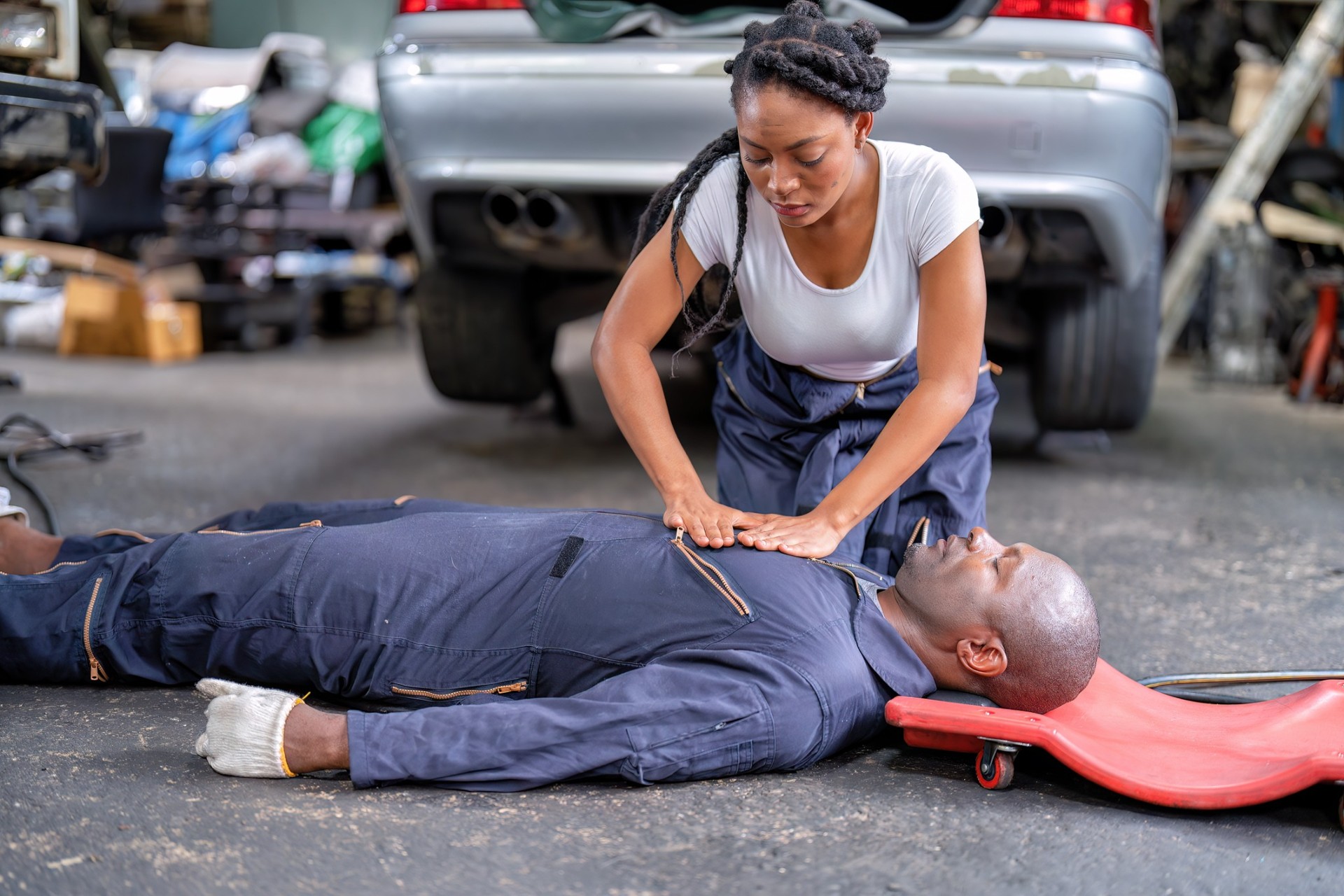 Female mechanic administering CPR to an unconscious coworker in a repair shop Female mechanic administering CPR to an unconscious coworker in a repair shop