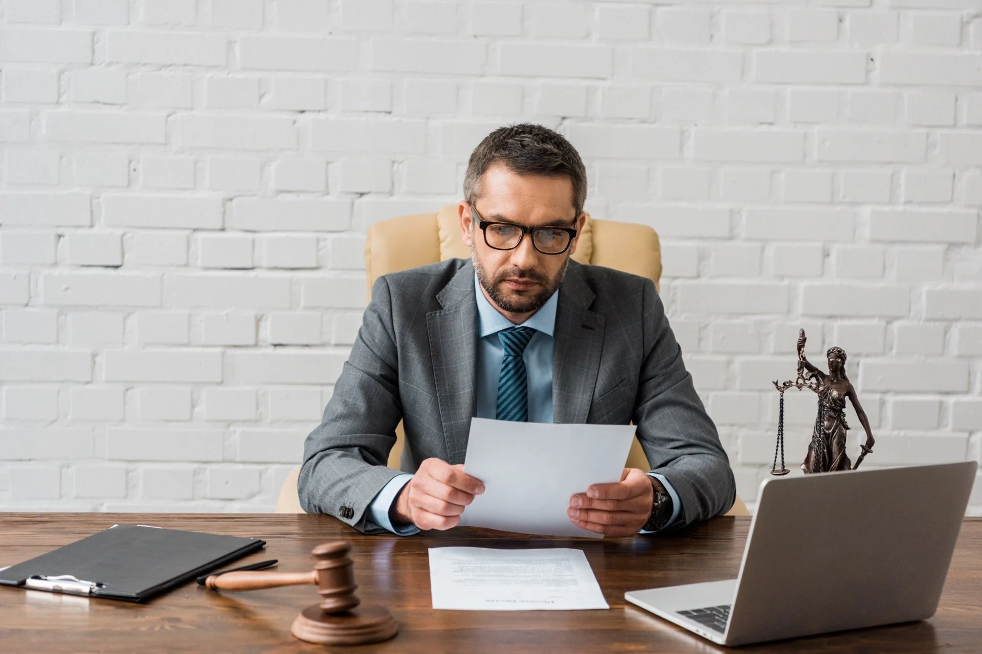 Male lawyer reading legal documents at his office desk with gavel and Lady Justice statue