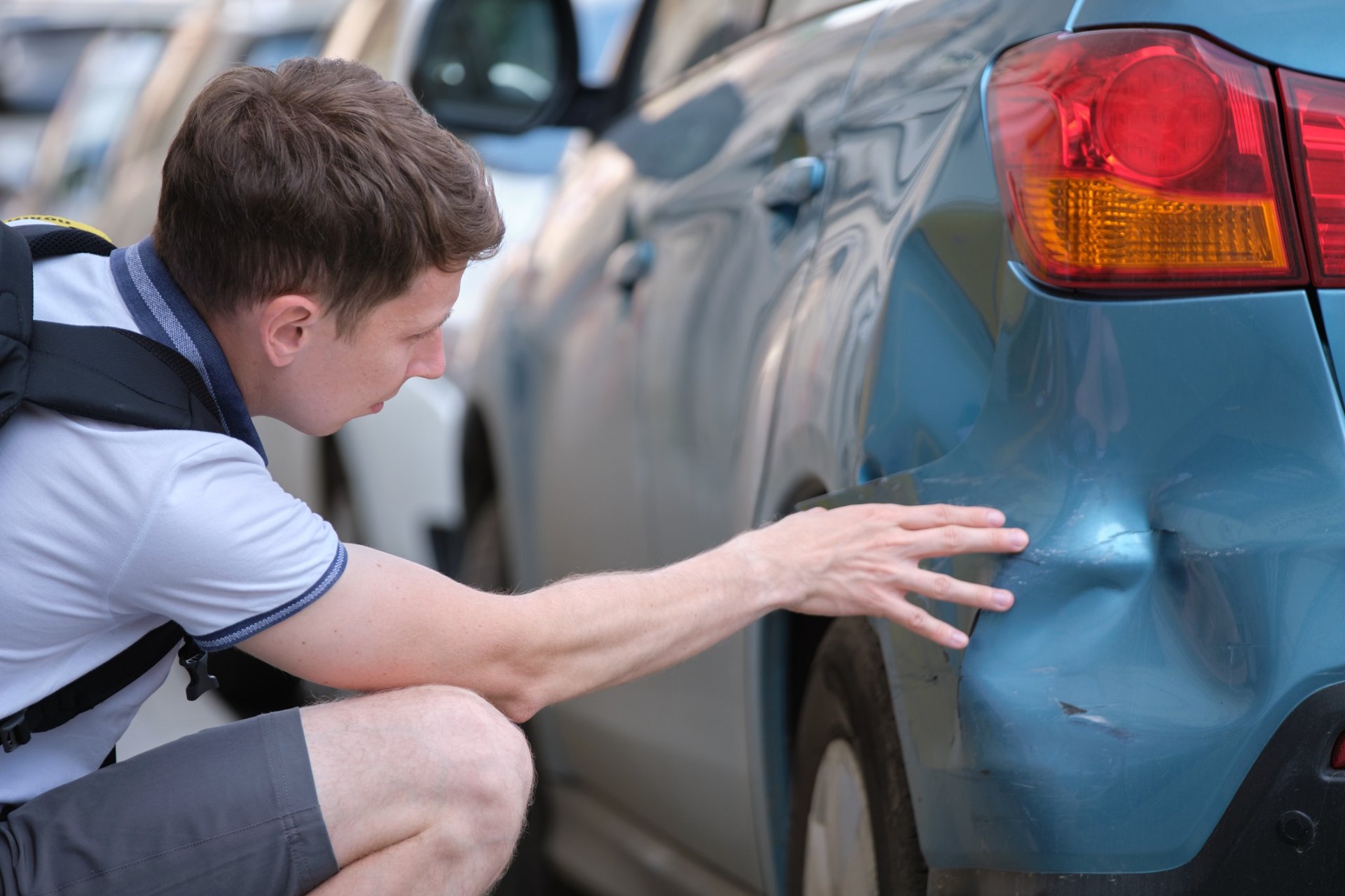 Man inspecting rear-end damage on a blue car after a minor accident