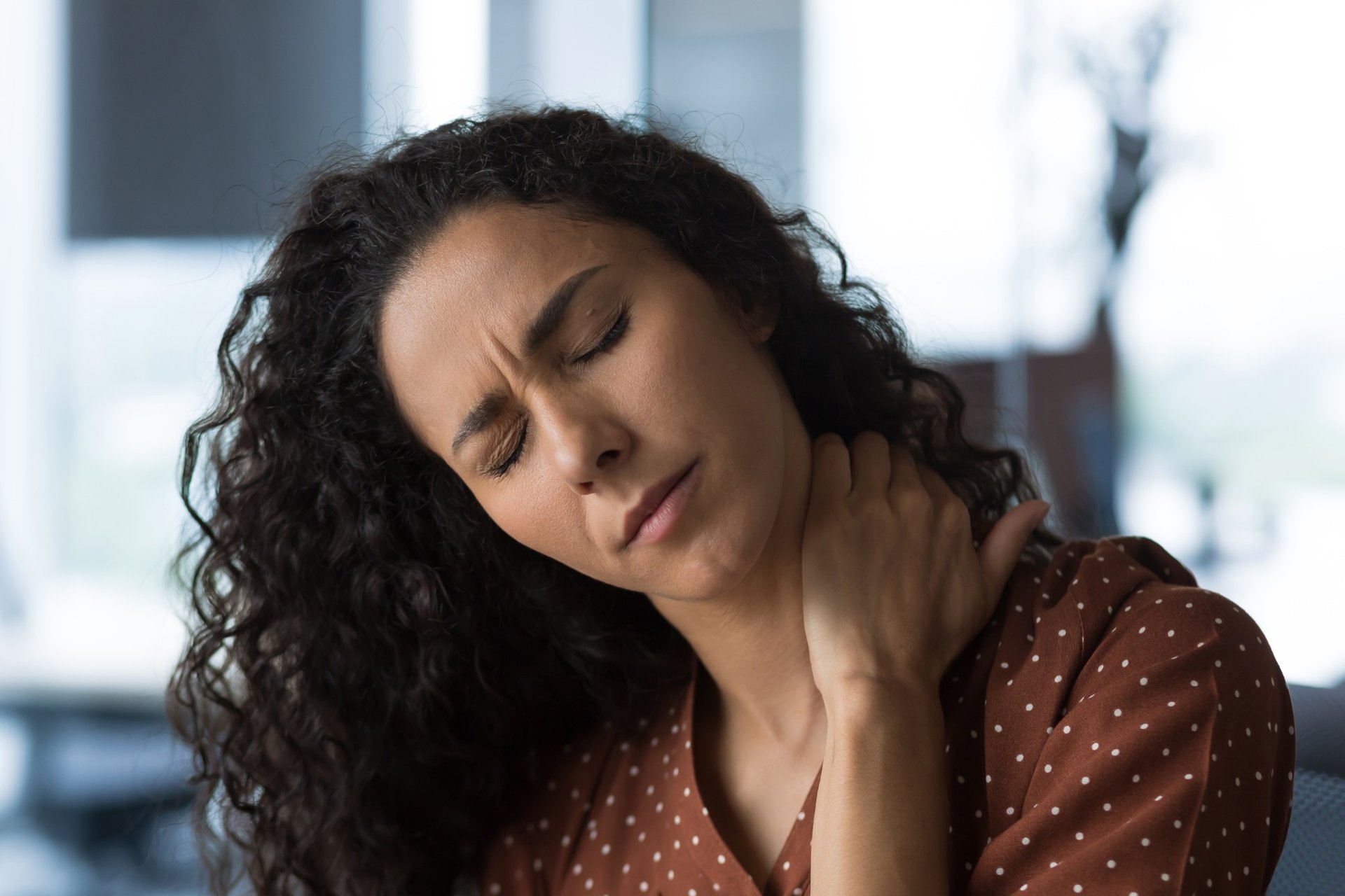 Woman with curly hair experiencing neck pain in an office setting