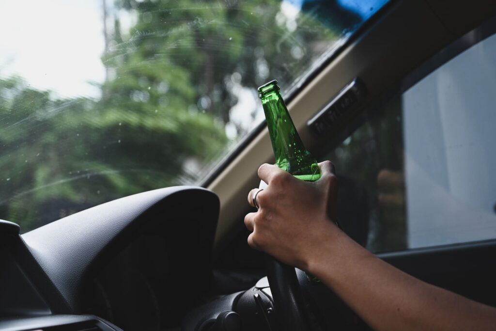 man drivin a car and holding bottle of beer