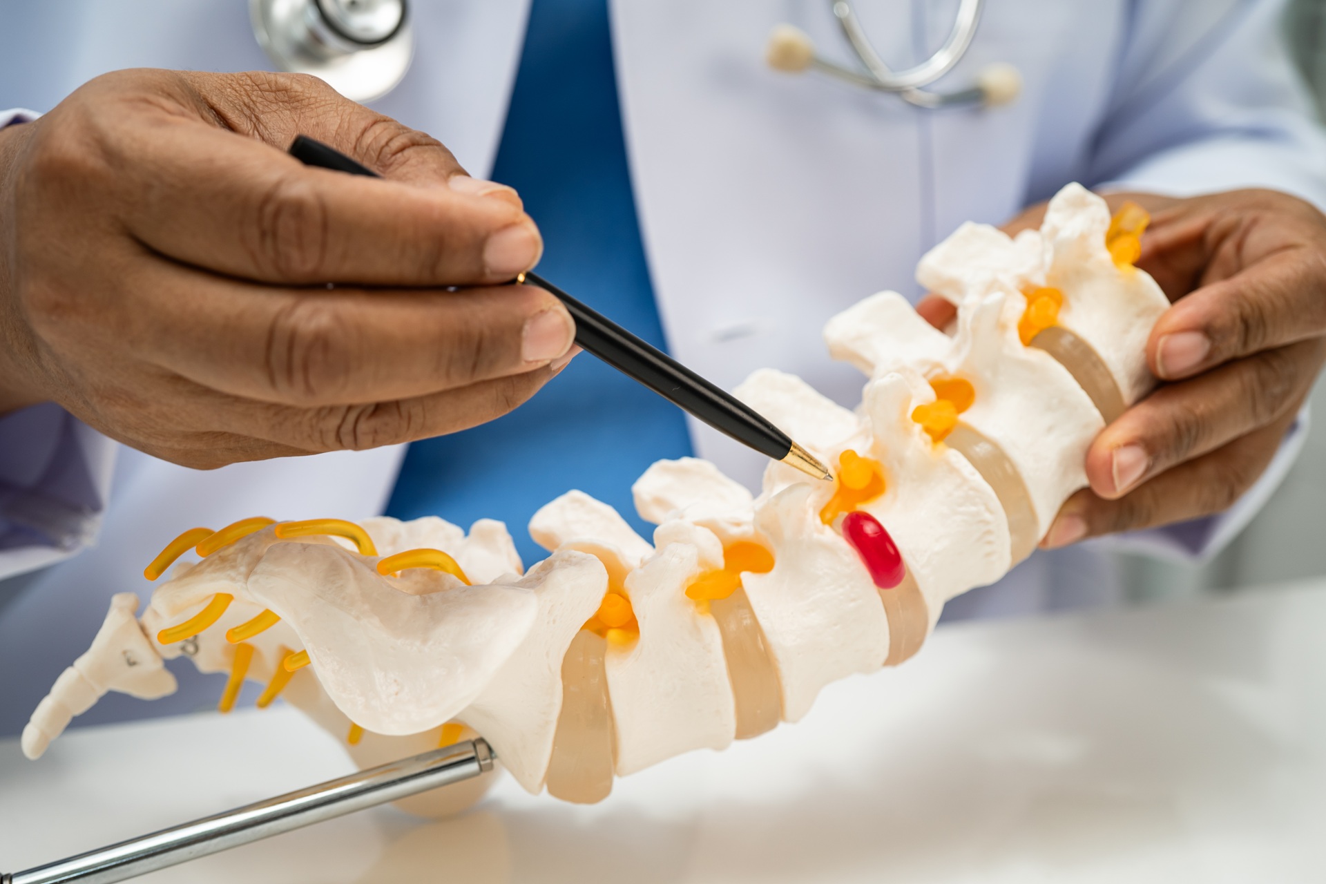 Male doctor holding and explaining a spinal X-ray to a female patient seated across the desk in a consultation room