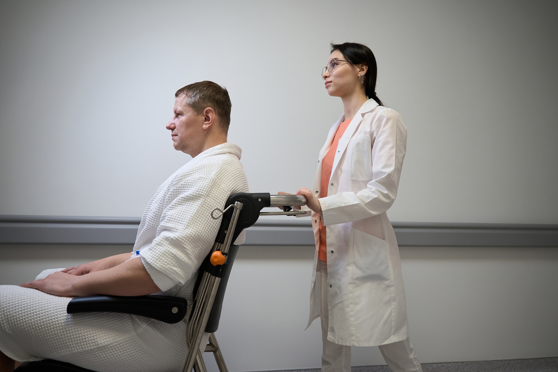 Medical professional pushing a male patient in a wheelchair along a hospital corridor