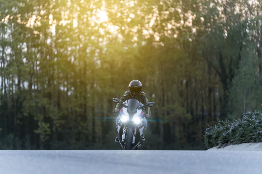 Motorcyclist riding sport bike on empty road with headlights on at sunset